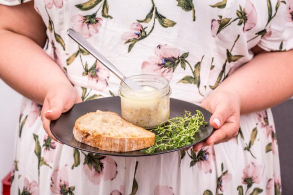 kobieta trzyma talerz z kromką chleba, smalcem z gęsi oraz z ziołami, nóż w słoiku